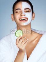 Laughing woman with the slice of cucumber in hand. Photo of funny girl with moisturizing facial mask. Beauty & Skin care concept