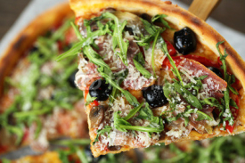 Fototapety Piece of pizza with arugula on wooden spatula,  close-up