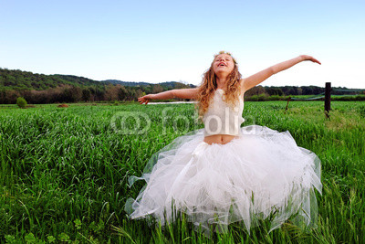 Cute girl with open arms in green grass field.