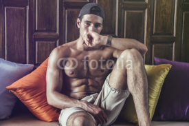 Shirtless athlete lying on pillows and looking at camera. Horizontal indoors shot.