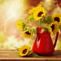 Fototapety Sunflower bouquet in jug on wooden table over autumn bokeh