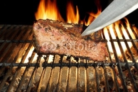 Chef Knife in the Grilled Meat Chop. Flame in Background.