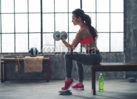 Obrazy i plakaty Fitness woman lifting dumbbell in urban loft gym