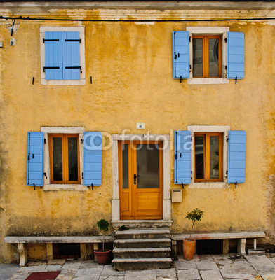 Front of an old house with blue shutters and yellow wall
