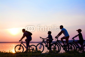Naklejki family on bicycles admiring the sunset on the lake. silhouette