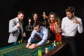 Group of young people behind roulette table on black background