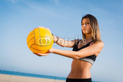 Beautiful beach volleyball female player serving ball.