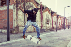 Naklejki young boy jumping with skateboard in outskirt street