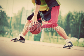 Fototapety Young man on basketball court dribbling with ball. Vintage mood