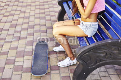 Beautiful hipster girl in a jeans shorts and pink shirt walking with skateboard near the green park, sexy style, adult, long legs, brunette, white shoes, sexy model,  posing on camera