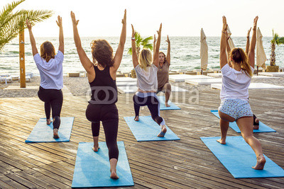 group of young females practicing yoga on the seaside during the sunrisе
