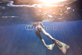 Naklejki Sexy woman with beautiful ass in a bikini swims in the ocean under water amid rays of the sun