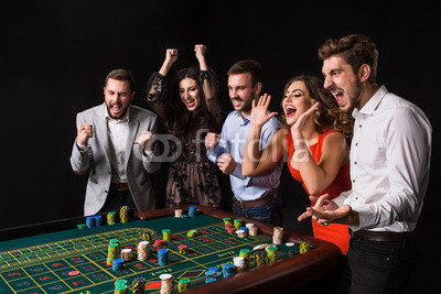 Group of young people behind roulette table on black background