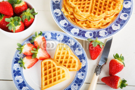 Crisp golden fresh baked waffle topped with strawberries on whit
