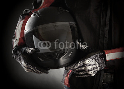 Motorcyclist with helmet in his hands. Dark background
