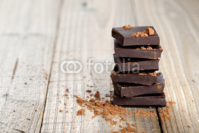 Pile of chocolate pieces with cocoa on wooden background