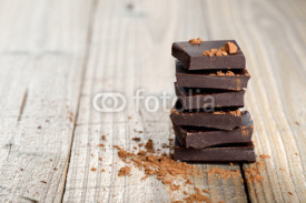 Naklejki Pile of chocolate pieces with cocoa on wooden background