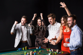 Group of young people behind roulette table on black background