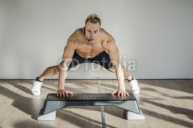 Young aerobics male coach shirtless leaning on step teaching class, looking at camera