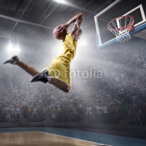 Fototapety Basketball player makes slam dunk on big professional arena. Player flies through the air with the ball. Player wears unbranded clothes.