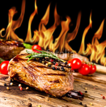 Naklejki Grilled beef steaks with flames on background
