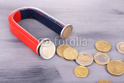 Magnet and coins on color wooden background
