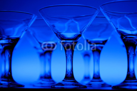 Naklejki Wineglasses arranged in rows on the table in blue light