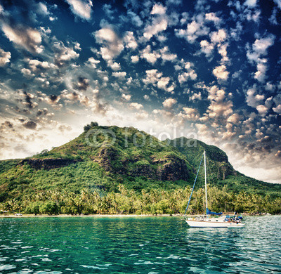 Polynesia. Island and vegetation at sunset with small boat on fo