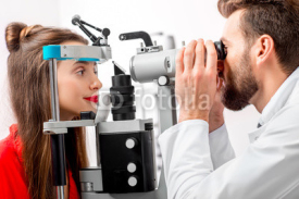 Eye doctor checking vision of young female patient with ophthalmologic device in the cabinet