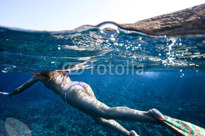 A woman floats on the background corals in thongs and flippers