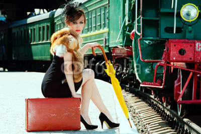 Retro girl sitting on suitcase at the train station