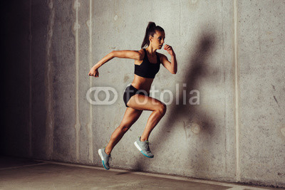 Slim attractive sportswoman running against a concrete background
