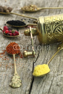 Old spoons with spices and pepper grinder on wooden background