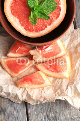 Part of ripe grapefruit in bowl, on wooden background