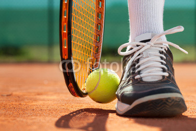 Legs of athlete near the tennis racket and ball