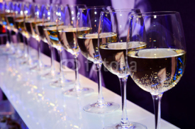 Naklejki Nightclub glasses with white wine lit by festive lights
