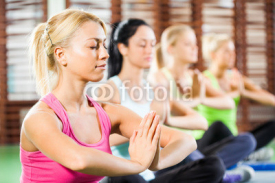 Naklejki Four girls meditating after fitness training in gym