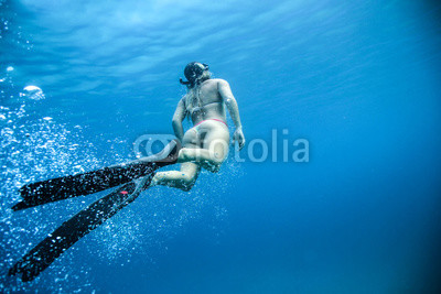 Woman underwater in the ocean with flippers and bubbles. Rear view of the beautiful butt