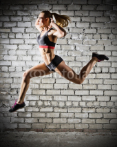 Naklejki Muscular jumping woman on brick wall background (dark version)