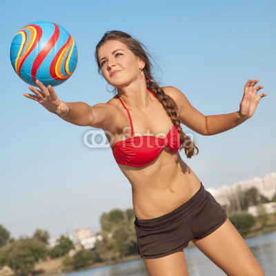 Young beautiful lady is playing volleyball on the beach