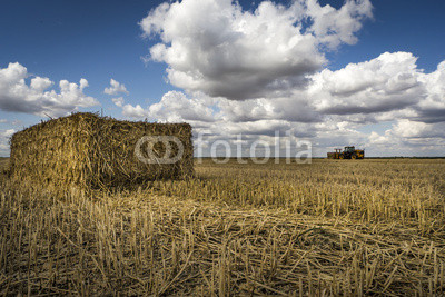 Straw bale, tractor on the horizon, fluffy cloud blue skies