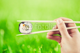 Naklejki Hand holding sushi roll using chopsticks