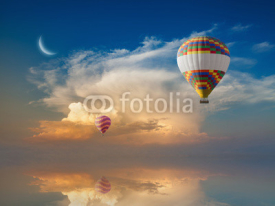 Hot air balloons flies in glowing sunset sky above calm sea