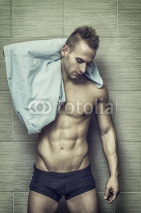 Handsome semi-naked muscular young man in bathroom with towel, looking at camera