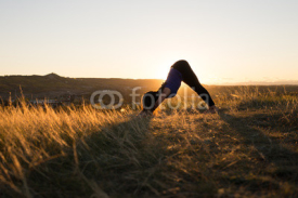 Woman doing yoga downward dog pose during sunset