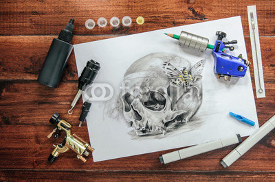 skull tattoo sketch with rotary machines, needles, grips on wooden background