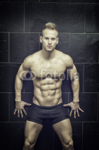 Handsome, muscular young man shirtless leaning against tiled wall, looking at camera