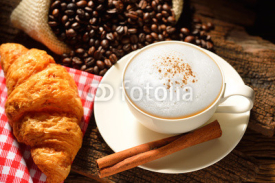 A cup of cappuccino with coffee beans and croissant