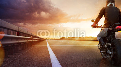 Biker riding motorcycle on an empty road at sunset
