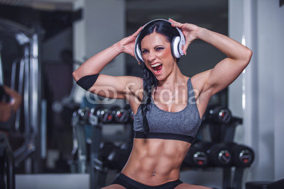 Crazy fit girl posing in gym with headphone.